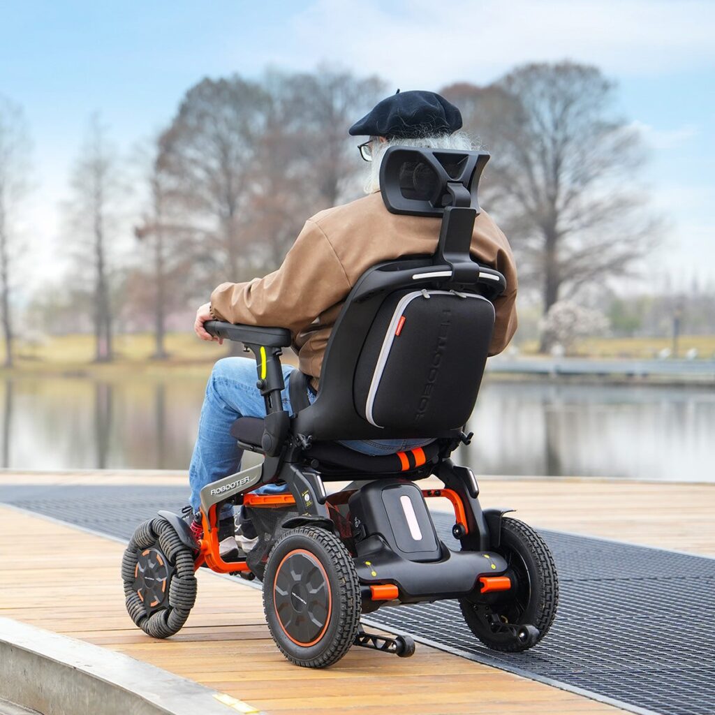 Rider on a Robooter E60 Pro GT crossing a wooden boardwalk by the water